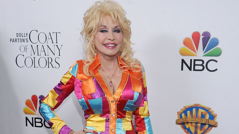 Dolly Parton singing on stage in a black and silver suit