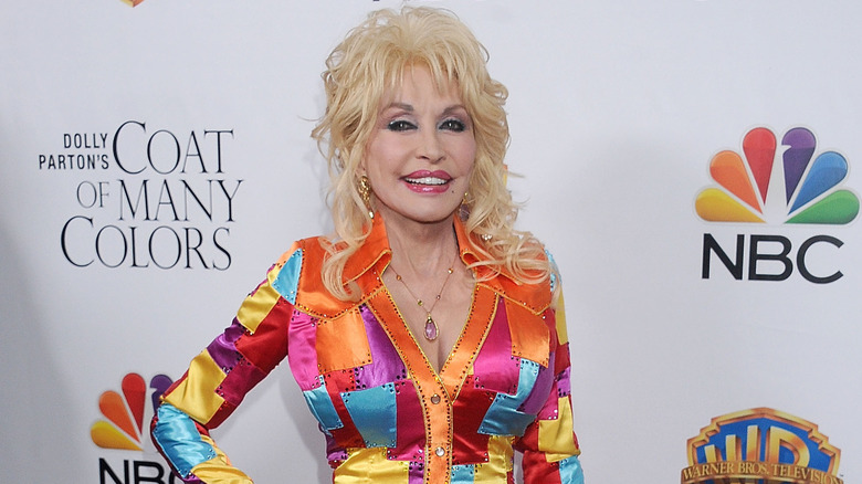 Dolly Parton singing on stage in a black and silver suit