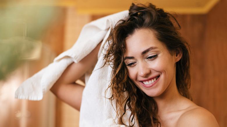 Woman drying hair with white towel smiling. 