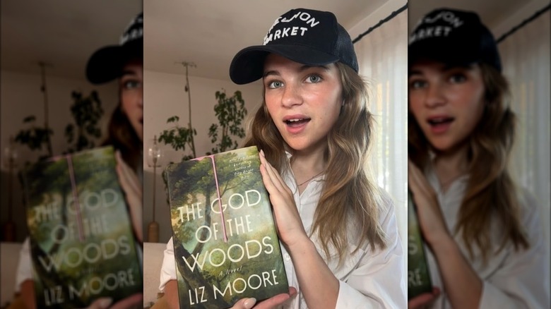 Raegan Revord posing with the book "The God of the Woods" by Liz Moore