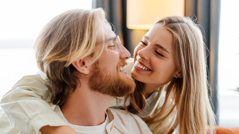 A blonde couple smiling at each other with the woman's arms around the man