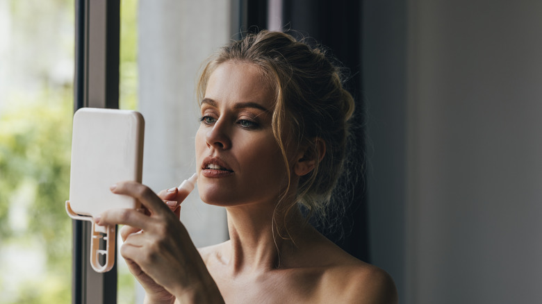 Woman applying makeup at window