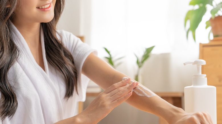 Woman sitting down in bathrobe applying lotion to bare arms