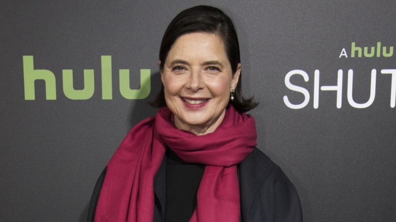 Isabella Rossellini smiling in front of a black background while wearing a pinks scarf