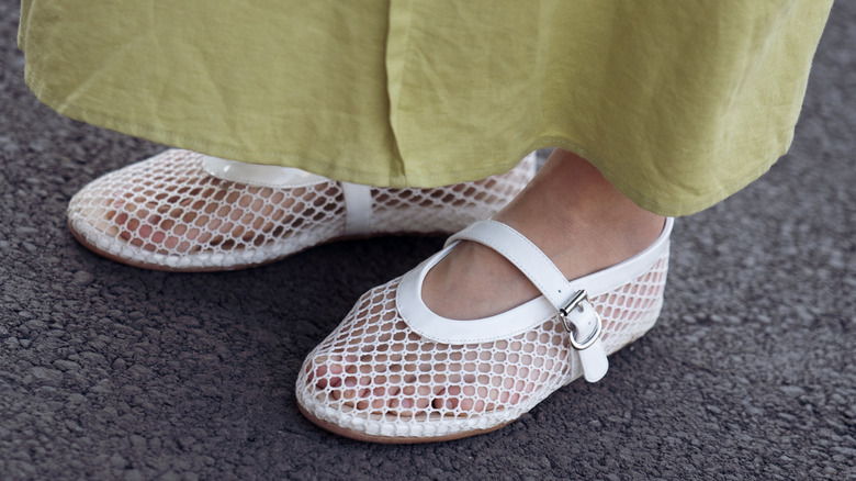 A close up a woman wearing a green skirt and white mesh flats with mary jane straps