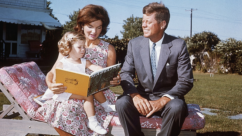 Jackie Kennedy with her husband and daughter reading a book outside