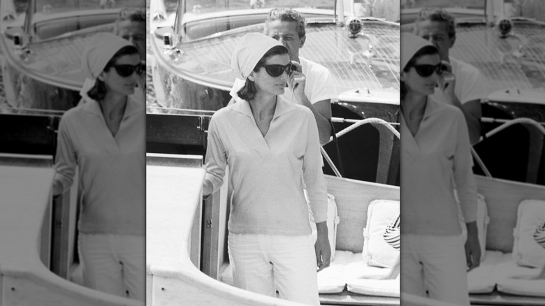 Jackie Kennedy in black and white on a boat wearing sunglasses and a head scarf
