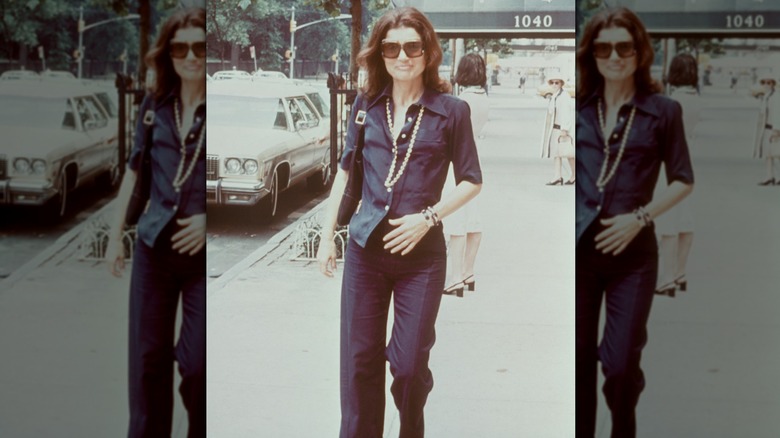 Jackie Kennedy in a long pearl neckace with a navy shirt and navy pants