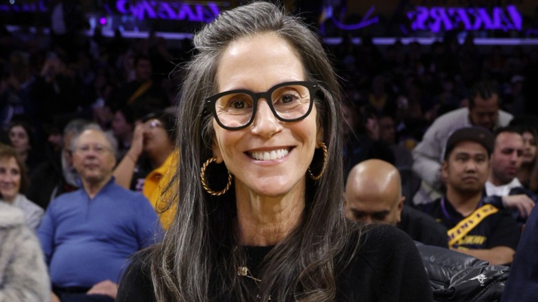 Jami Gertz smiling at a basketball game with long, dark gray hair