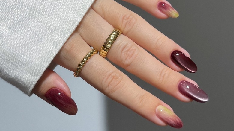 An open hand featuring cateye nails with different shades of dark berry alongside accent nails of berry and light green