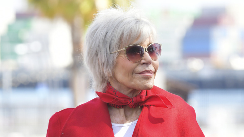 Jane Fonda with gray hair and a red coat and scarf at an event in California