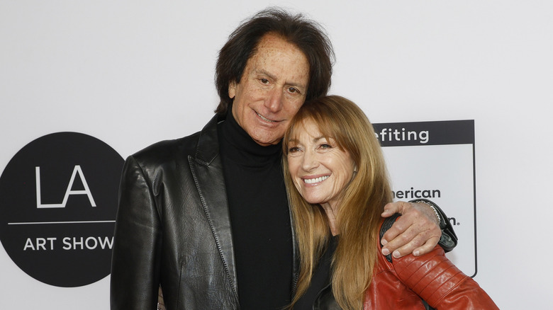 John Zambetti and Jane Seymour hug in front of a step-and-repeat