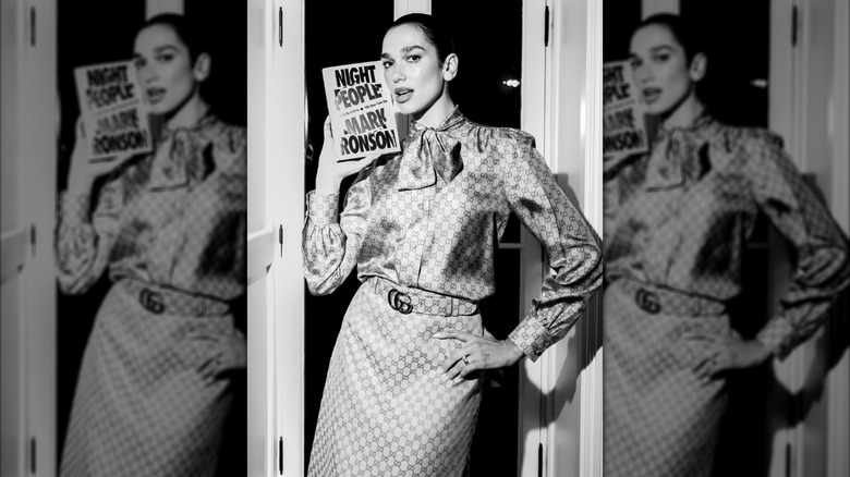 A black and white photo of Dua Lipa posing with a copy of "Night People"