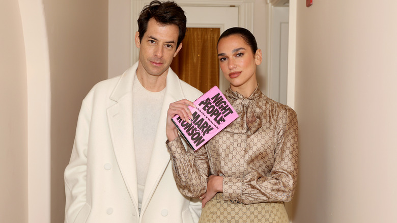 A person reading a book and holding a cup of tea in front of a fireplace