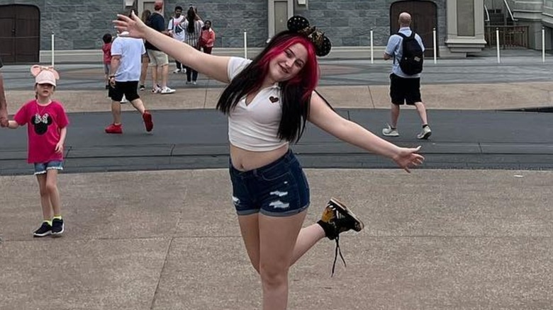 Bailee Ann DeFord posing at Disneyland in a crop top and jeans shorts with black and pink hair