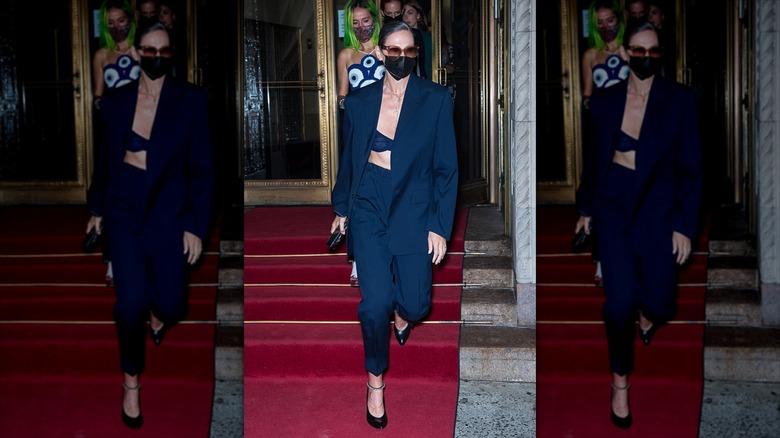 Jenna Lyons walks wearing a mask and a three-piece navy suit
