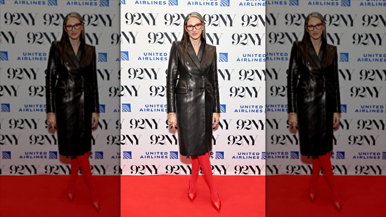Jenna Lyons poses with her legs crossed wearing a long leather jacket and red tights