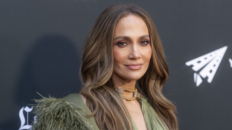 Jennifer Lopez smiling on the red carpet in front of a dark gray background