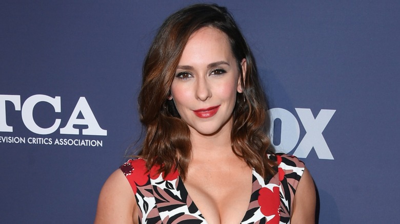 Jennifer Love Hewitt smiling on the red carpet in a plunging floral dress with red lipstick