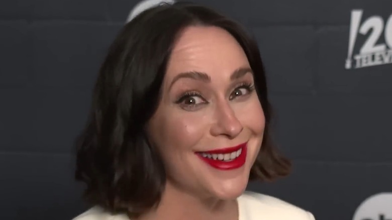 Jennifer Love Hewitt smiling on the red carpet with a dark brunette bob and red lipstick at a 9-1-1 event in 2024