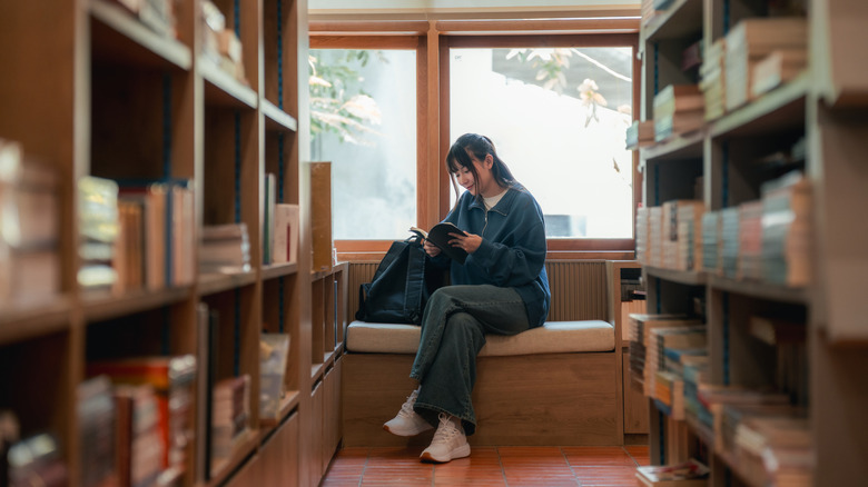 Young woman sitting on a bench at a bookstore, reading a short book