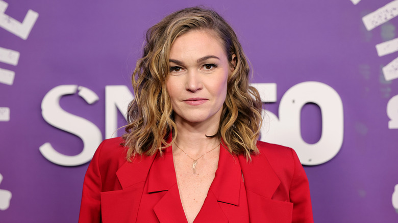 Julia Stiles poses wearing a vibrant red blazer and waistcoat