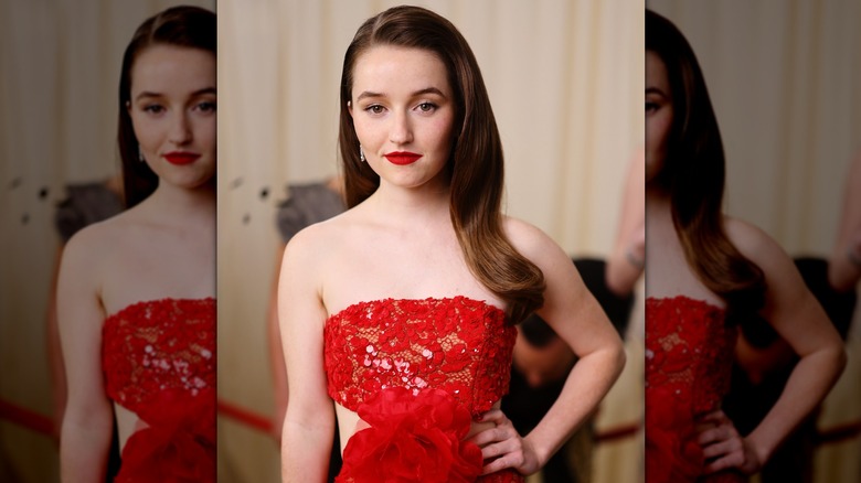 Kaitlyn Dever posing in a red gown with a side-parted hairstyle