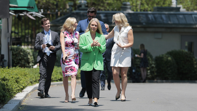 Karoline Leavitt walking outside in a green blazer and black pants