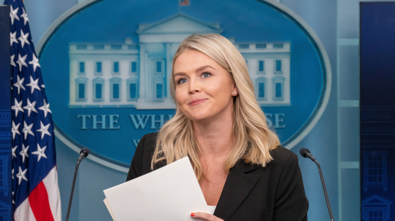 Karoline Leavitt standing at a podium and holding papers