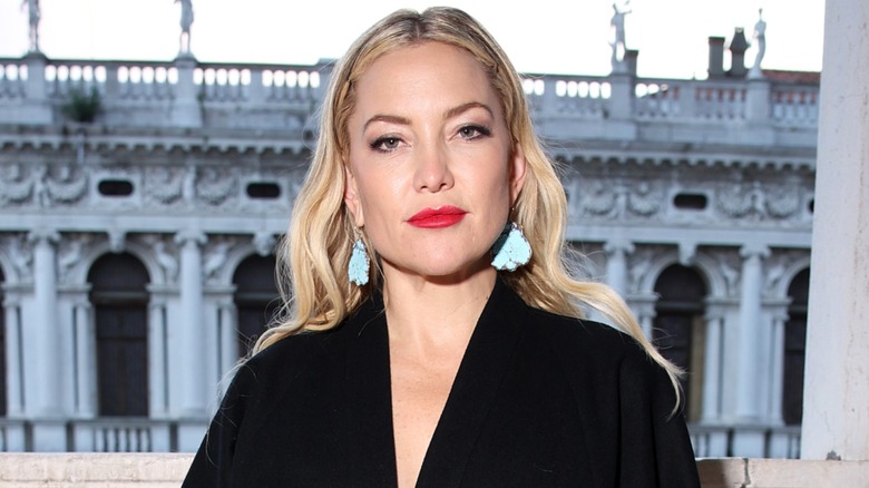 Kate Hudson posing in front of an old building wearing red lipstick