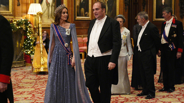 Kate Middleton in a blue sequin dress at an event talking to a man