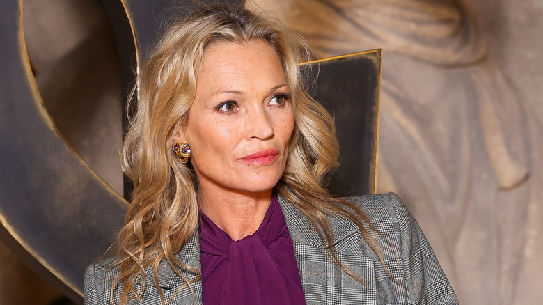 Kate Moss looking off-camera while wearing a purple blouse and tweed blazer