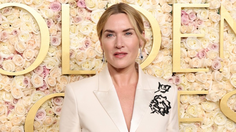 Kate Winslet posing in front of a flower wall at the 2025 Golden Globe Awards in a white suit