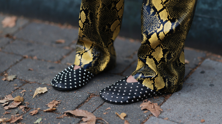 Person wearing studded ballet flats and snakeskin trousers