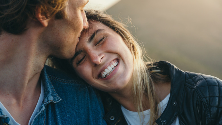 Man kissing smiling woman on the head outdoors