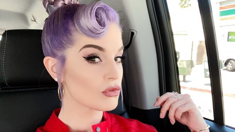 Kelly Osbourne posing in a car in 2020, with her purple hair in an updo