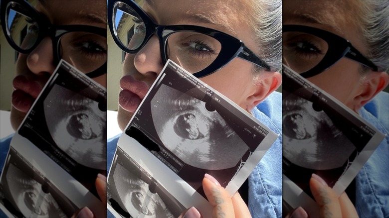 Kelly Osbourne posing for a selfie, holding sonogram scans