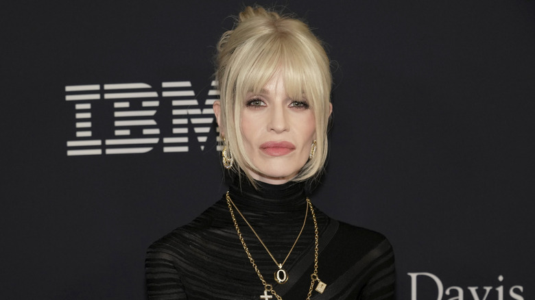 Kelly Osbourne posing at the Pre-Grammy Gala while wearing a black, high-necked dress and blond hairstyle with bangs