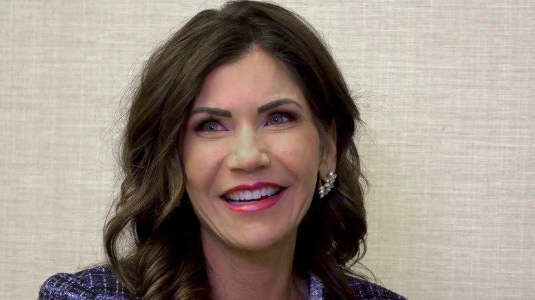 Kristi Noem in a blue tweed blazer with diamond earrings smiling
