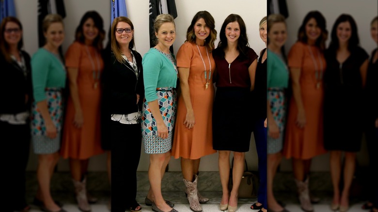 Kristi Noem, in tangerine short-sleeved dress, surrounded by doctors and students of the American Optometric Association, at Capitol Hill in 2017