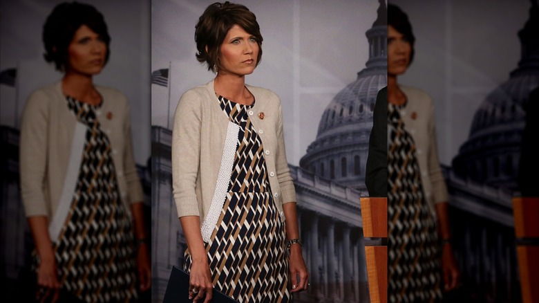 Kristi Noem, in short beige cardigan and geometric-patterned dress, at a news conference on Capitol Hill in 2013