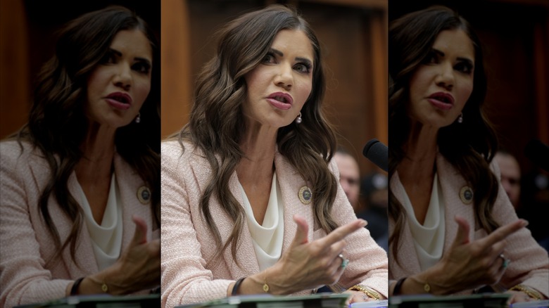 Kristi Noem speaking while seated at a desk in a pale pink suit