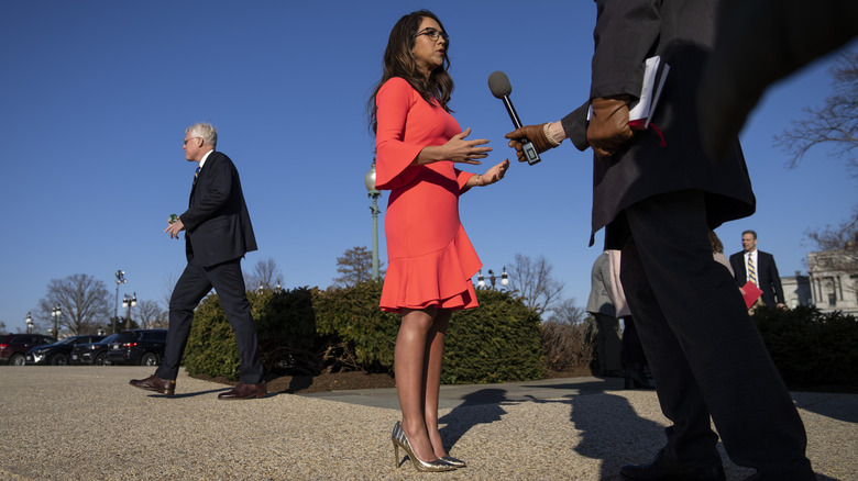 Lauren Boebert in a coral wrap dress, talking to a reporter