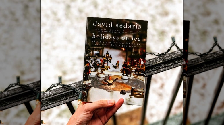 A hand holding up "Holidays On Ice" in front of an iron fence