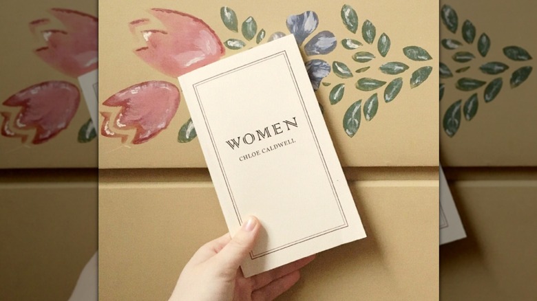 A hand holding up "Women" in front of a yellow wall