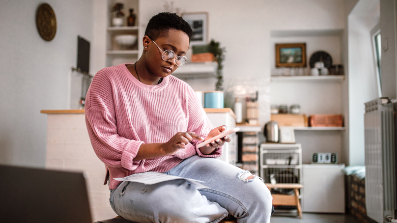 Woman holds phone while sitting on living room table