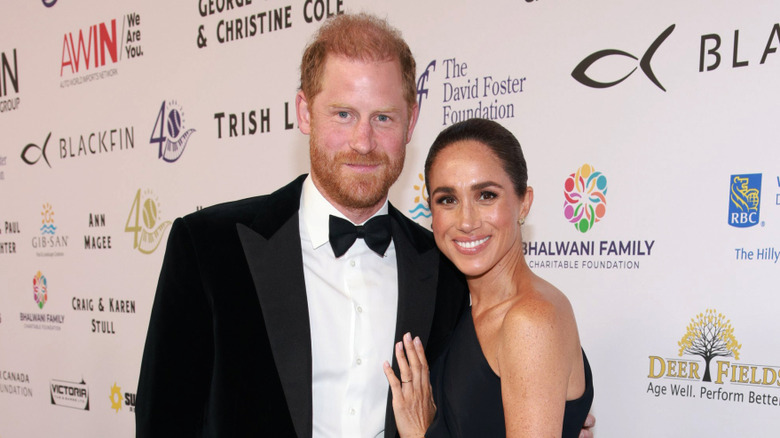 Prince Harry and Meghan Markle standing close on a red carpet at an event