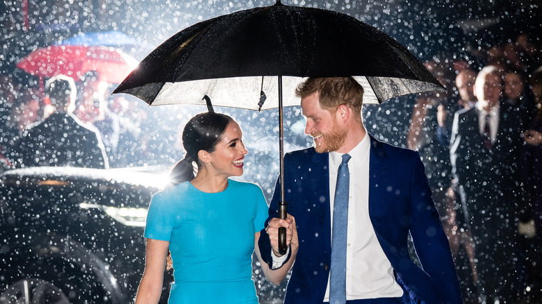 Meghan Markle in a blue dress walking in the rain with Prince Harry in a blue suit