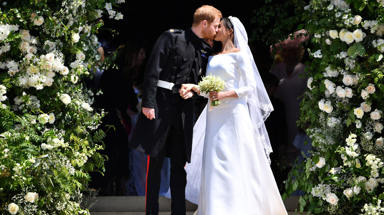 Prince Harry kissing Meghan Markle on their wedding day surrounded by flowers