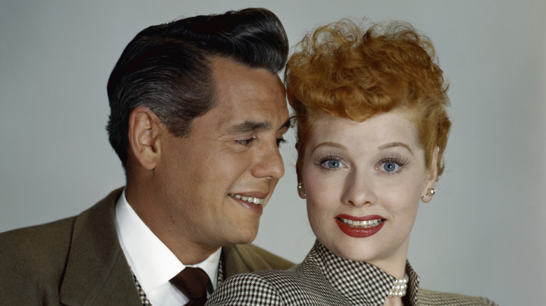 Lucille Ball and Desi Arnaz pose for a photo while he looks at her and she looks at the camera